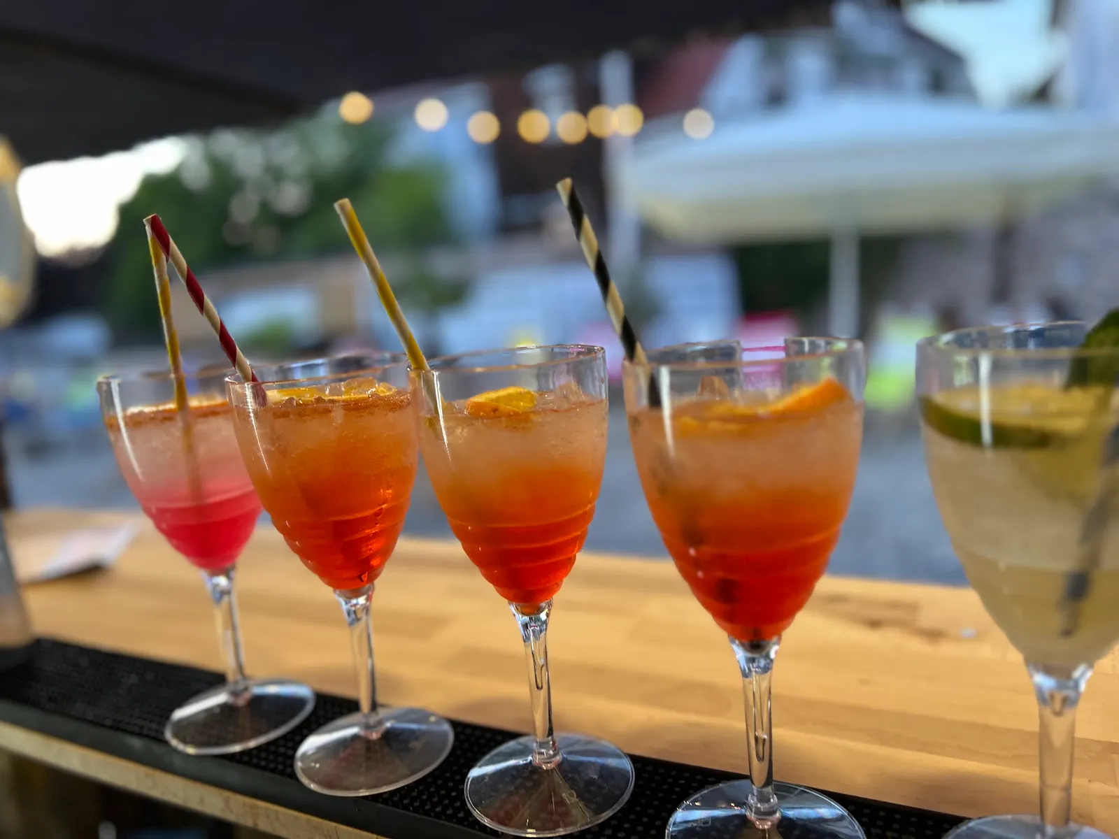 Fünf frisch gemixte Cocktails auf der Holztheke im Abendlicht