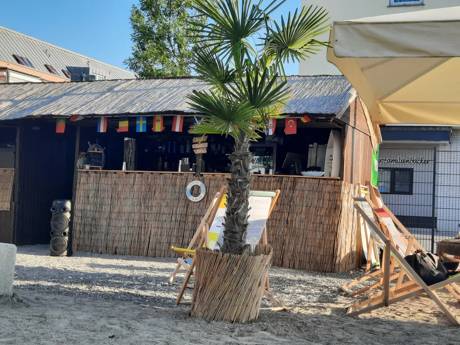 Die Beachbar Aroma del Sol mit Palme, Liegestühlen im Sand und der flaggengeschmückten Theke