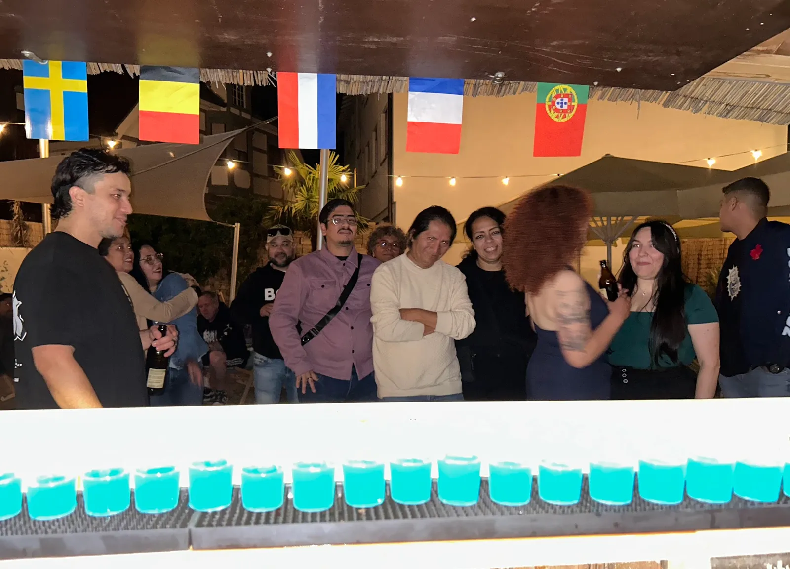 Reihe blau leuchtender Shots auf der Theke bei Nacht mit feiernden Gästen